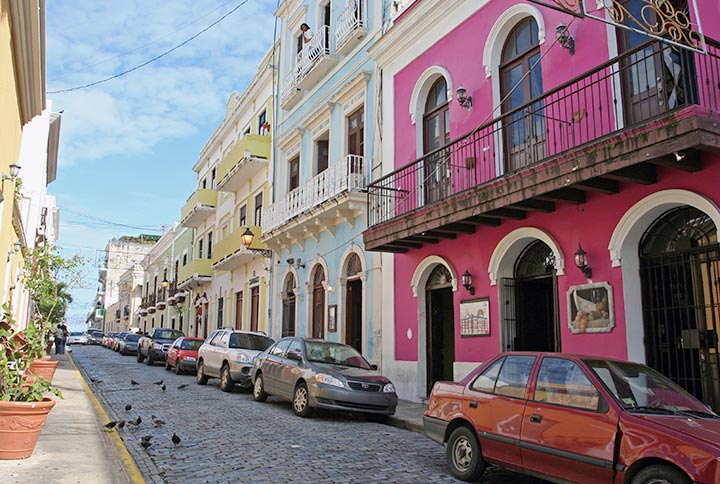 A city street in Puerto Rico with parked cars and a vibrant pink row house